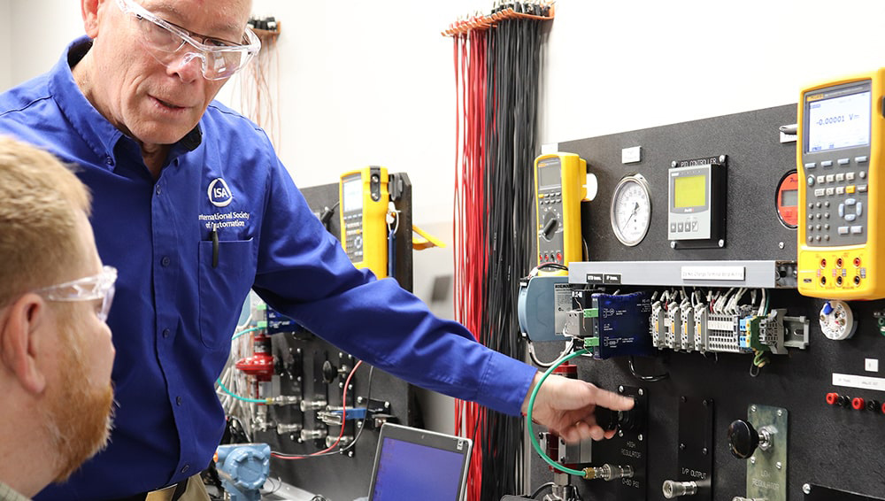 Course instructor wearing safety glasses teaching student how to use lab instrumentation training board